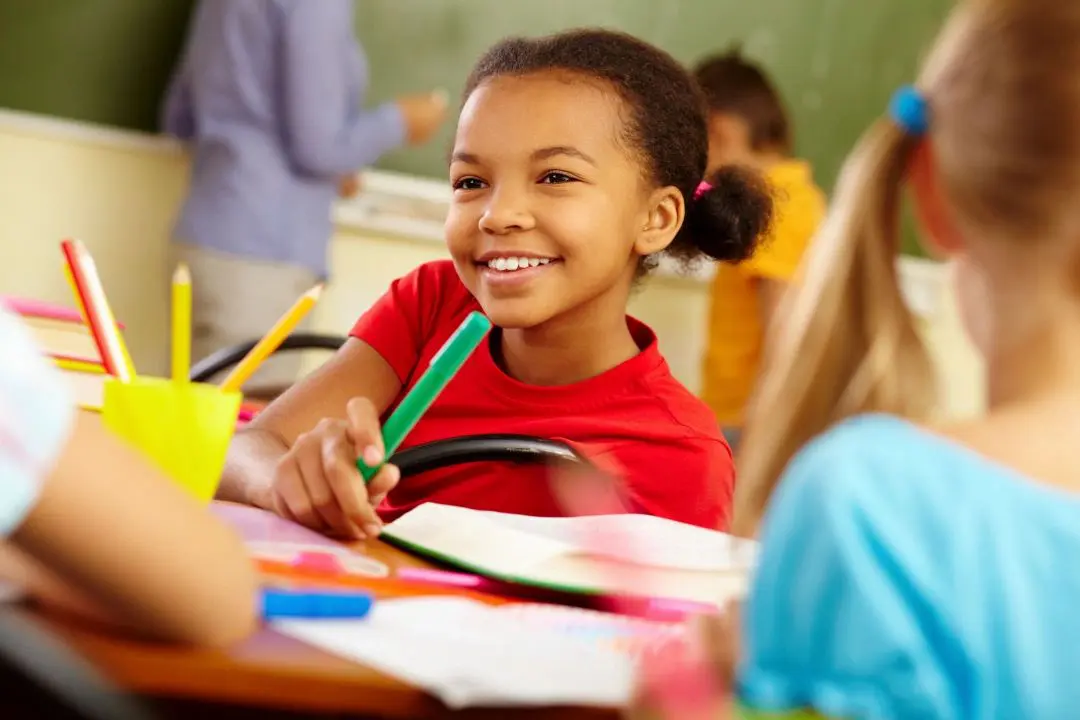 A young girl smiles while holding onto a green pencil.