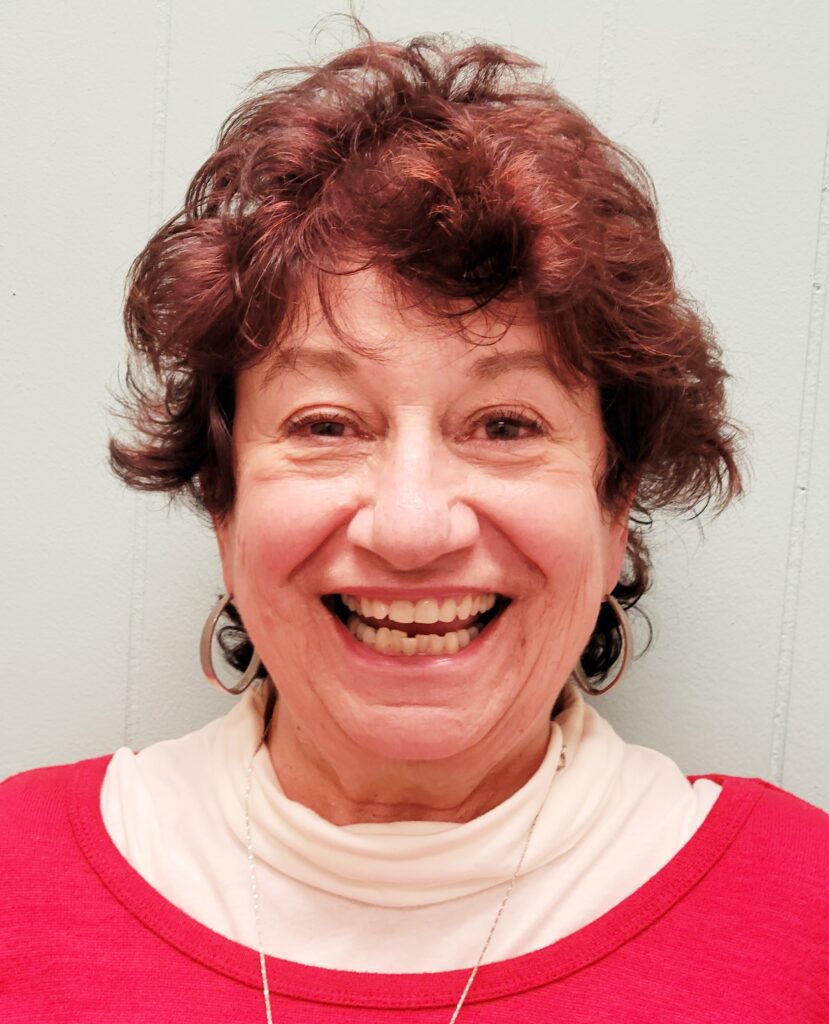 A woman with red hair and a white shirt is smiling.